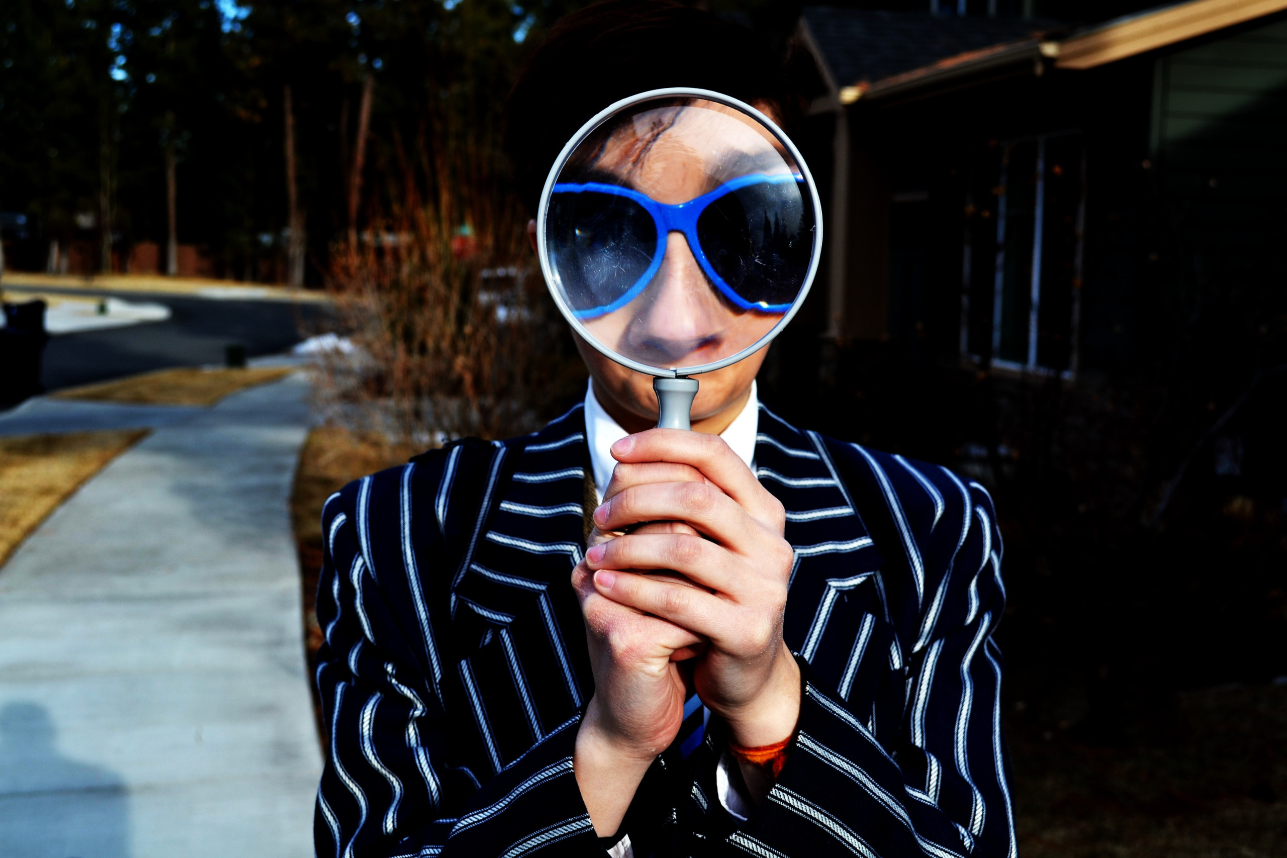 A lady holding a magnifying glass up to her head and her face is blown up and shows her sunglasses.