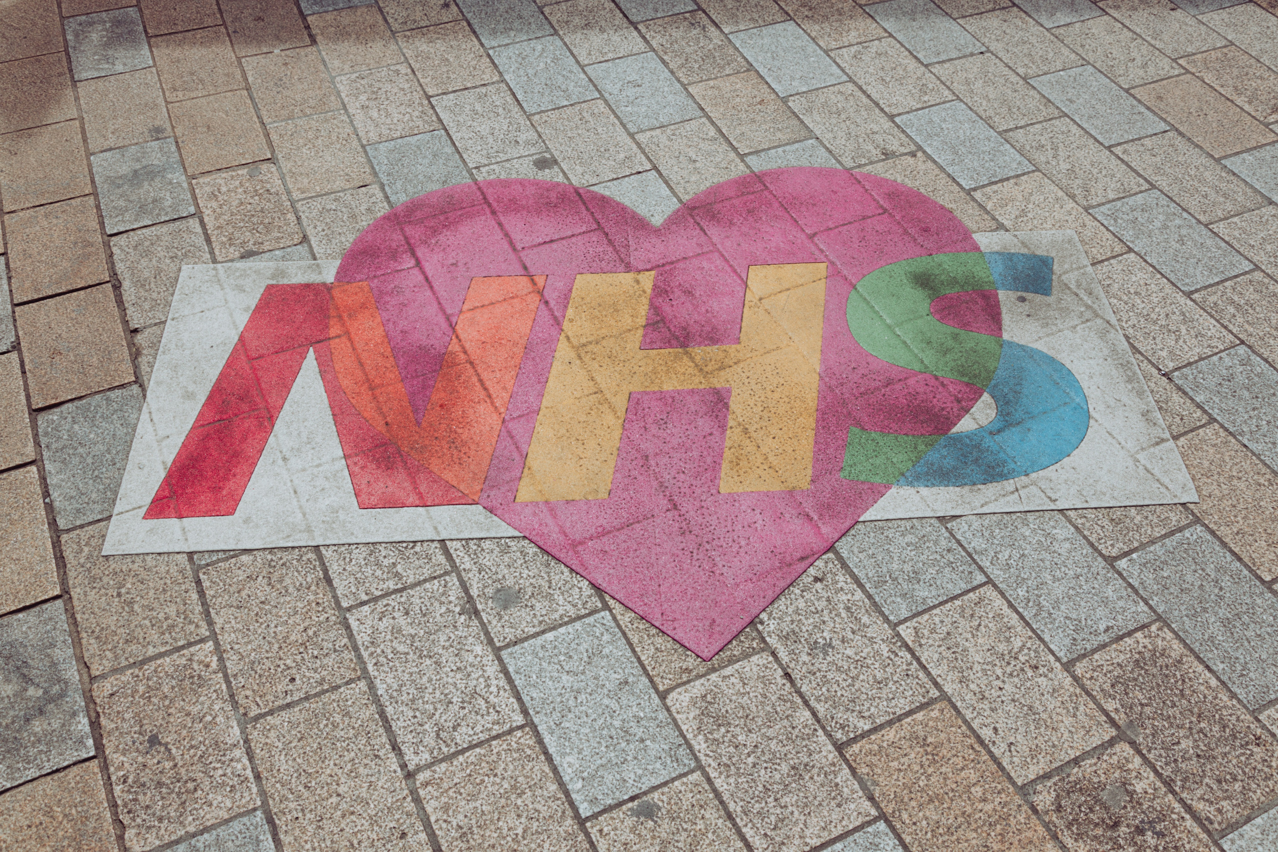 NHS sign with a heart around it drawn on a brick drive way.